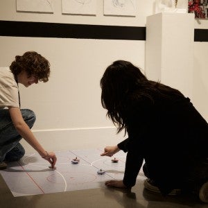 Two students play with spinning tops on the floor.