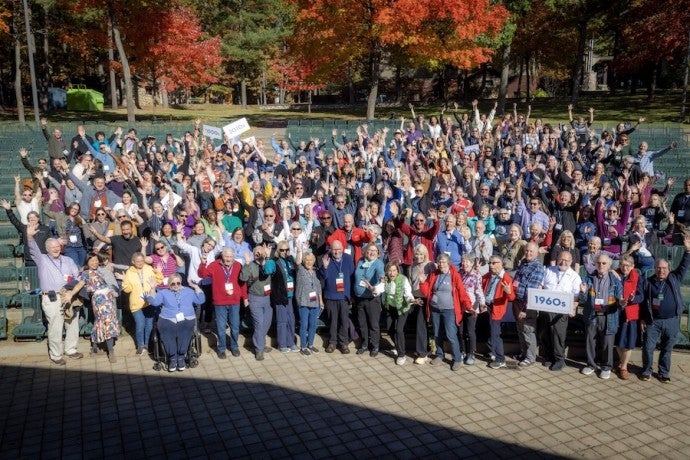 A large group of excited alumni smile and wave their hands.